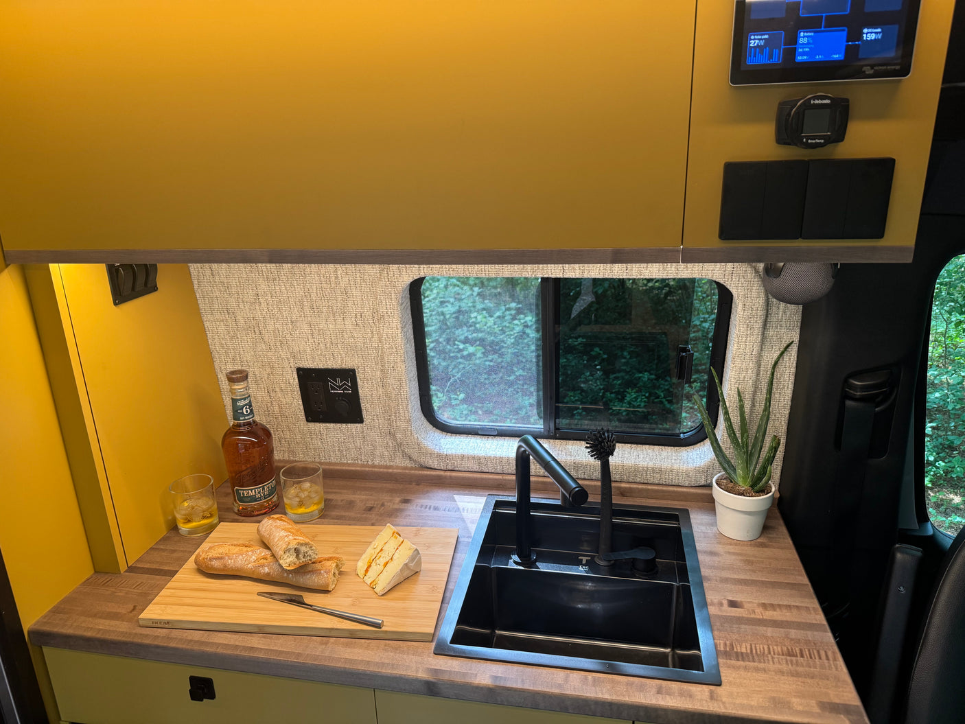 Comfortable RV rental kitchen with energy monitor, whiskey, and cheese for a cozy mobile living experience.