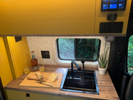 Comfortable RV rental kitchen with energy monitor, whiskey, and cheese for a cozy mobile living experience.