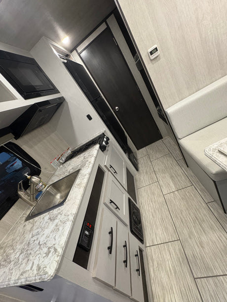 Modern RV rental kitchen with sink, microwave & stovetop, next to a comfy dinette area. Light, bright interior.