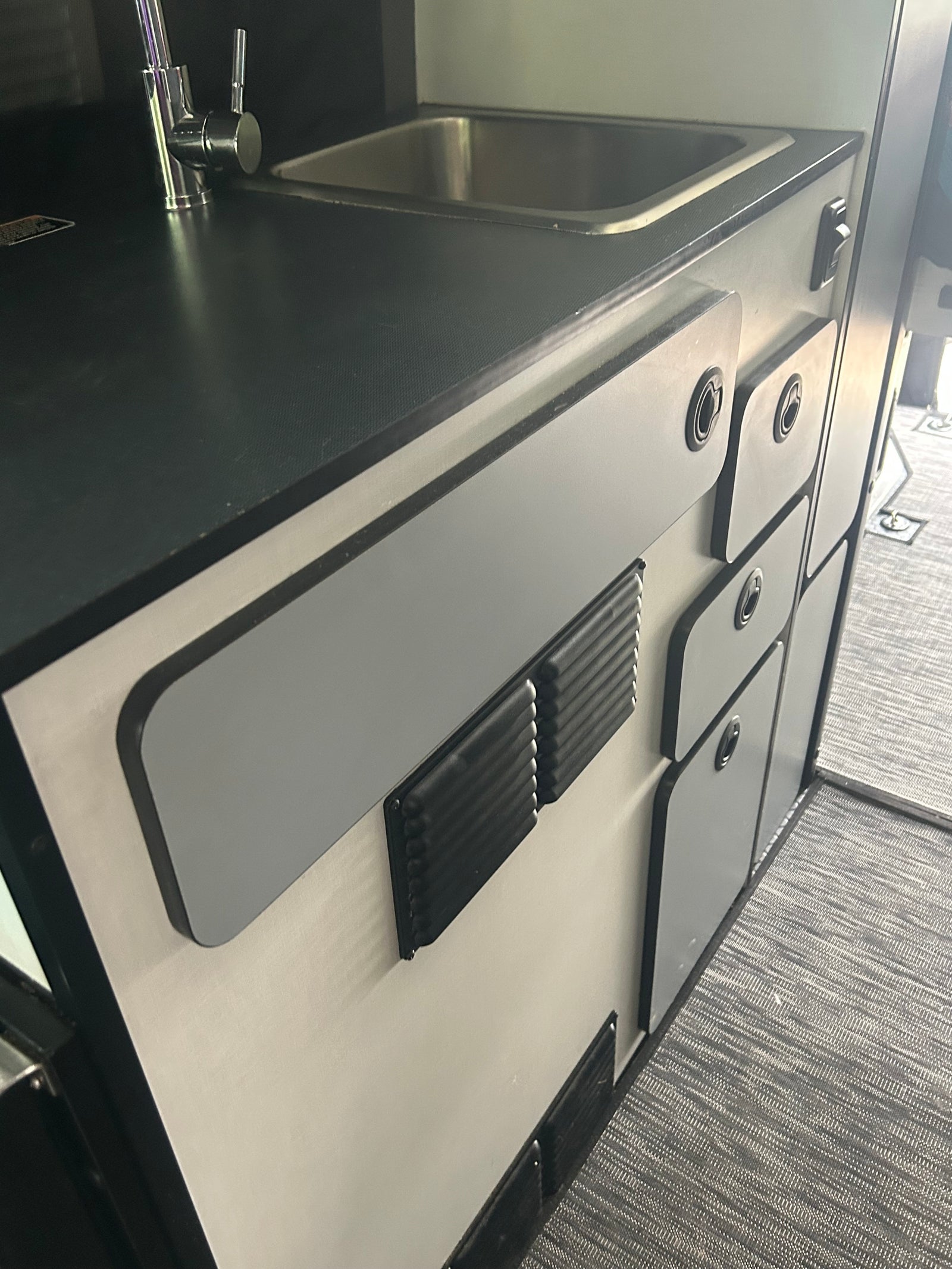 Compact RV rental kitchenette featuring a sink, faucet, and practical storage cabinets. Ideal for camper living.