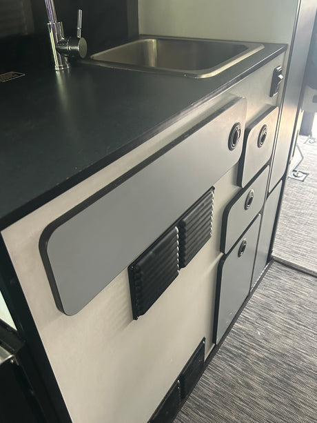 Compact RV rental kitchenette featuring a sink, faucet, and practical storage cabinets. Ideal for camper living.