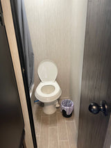 Inside an **rv rental**: a compact bathroom with a white toilet, grey shower curtain, trash bin, and tiled floor.