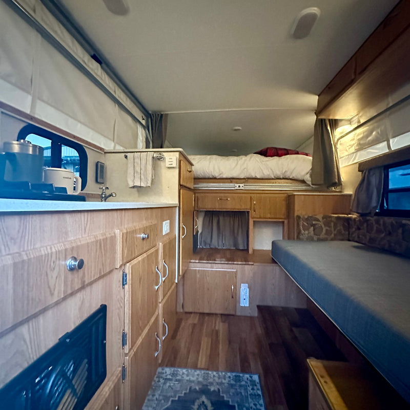 is parked for breathtaking mountain views under dramatic clouds.|An RV rental truck camper at a peaceful forest campsite among tall trees — photo 8