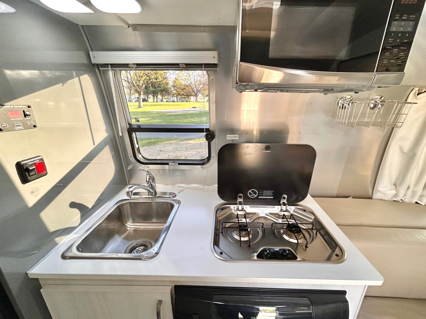 RV rental kitchen: stainless steel sink, two-burner stove, microwave, and scenic outdoor view. — photo 8
