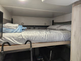 Inside an RV rental, a comfy bunk bed with grey sheets and a blue blanket. A ladder provides access to the sleeping area.