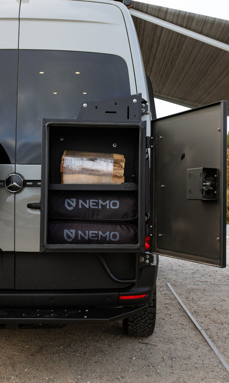 An rv rental's exterior storage: a rugged box open on the back of a van, holding firewood & two NEMO gear bags.