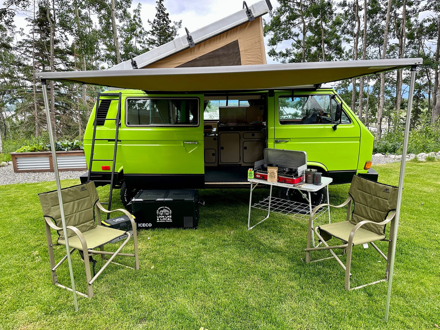 Bright green VW camper van, ideal for RV rental adventures, with awning, chairs, and cooking setup for outdoor living.