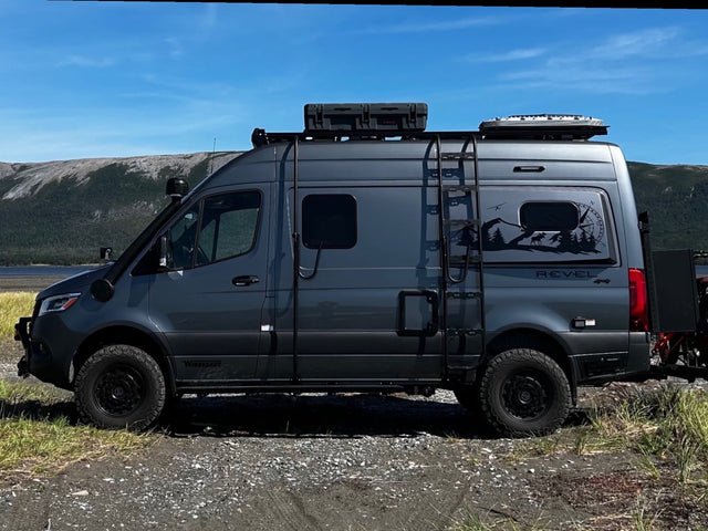Grey Winnebago Revel 4x4 adventure van with off-road tires & roof rack parked by mountains. Great rv rental for exploration!|RV rental parked on a sandy beach with electric bikes. A heart in the sand reads "Geoff & Tracey Newfoundland 2024."|Cozy RV rental morning: plaid blankets