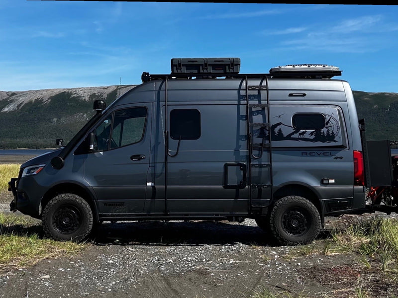 Grey Winnebago Revel 4x4 adventure van with off-road tires & roof rack parked by mountains. Great rv rental for exploration!|RV rental parked on a sandy beach with electric bikes. A heart in the sand reads "Geoff & Tracey Newfoundland 2024."|Cozy RV rental morning: plaid blankets — photo 1