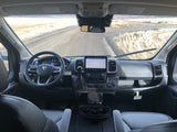 Interior of an rv rental van cockpit, showing the steering wheel, infotainment screen, and a dirt road view.