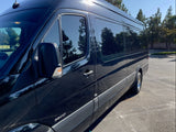 Black Sprinter van side profile, ready for your RV rental journey. Tinted windows reflect surrounding trees and sky.