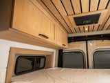 Inside an RV rental: light wood cabinets, slatted ceiling with vent, cozy bed, and side windows.