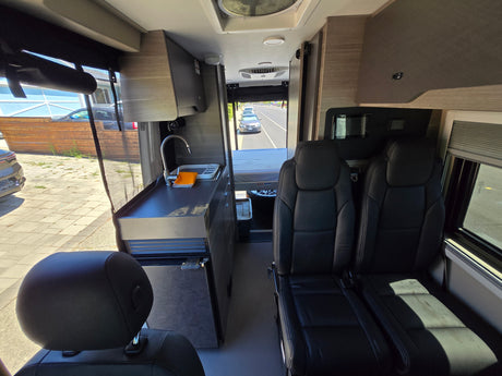 Bright interior of an rv rental, showing the galley kitchen, comfortable seating, and cozy bed in a compact layout.