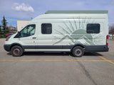Light green RV rental camper van with mountain/sun graphic parked on asphalt under a partially cloudy sky.