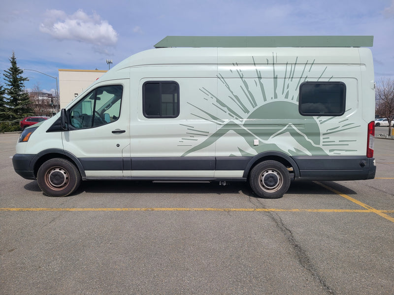 Light green RV rental camper van with mountain/sun graphic parked on asphalt under a partially cloudy sky. — photo 1
