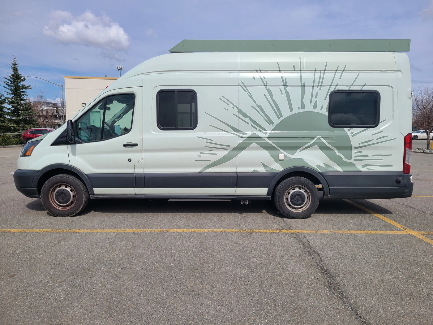 Light green RV rental camper van with mountain/sun graphic parked on asphalt under a partially cloudy sky.|Spacious RV rental bedroom featuring a patterned bed — photo 21