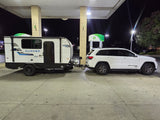 RV rental adventure: White Jeep Grand Cherokee towing a Clipper travel trailer at a brightly lit BP gas station at night.