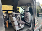 Inside a gray RV rental van, highlighting a child car seat, portable fridge on a stand, and seat-back organizer.