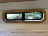 Inside an RV rental: A long, wood-framed window overlooks vibrant green plants and foliage.