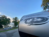 Lakeside bliss with our RV rental! The front of a 'Wolf Pup' travel trailer, parked by water, trees & a picnic table.