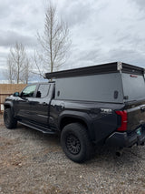 This dark grey Toyota Tacoma truck with a GFC overland camper, equipped with rugged tires, is ready for an RV rental adventure.