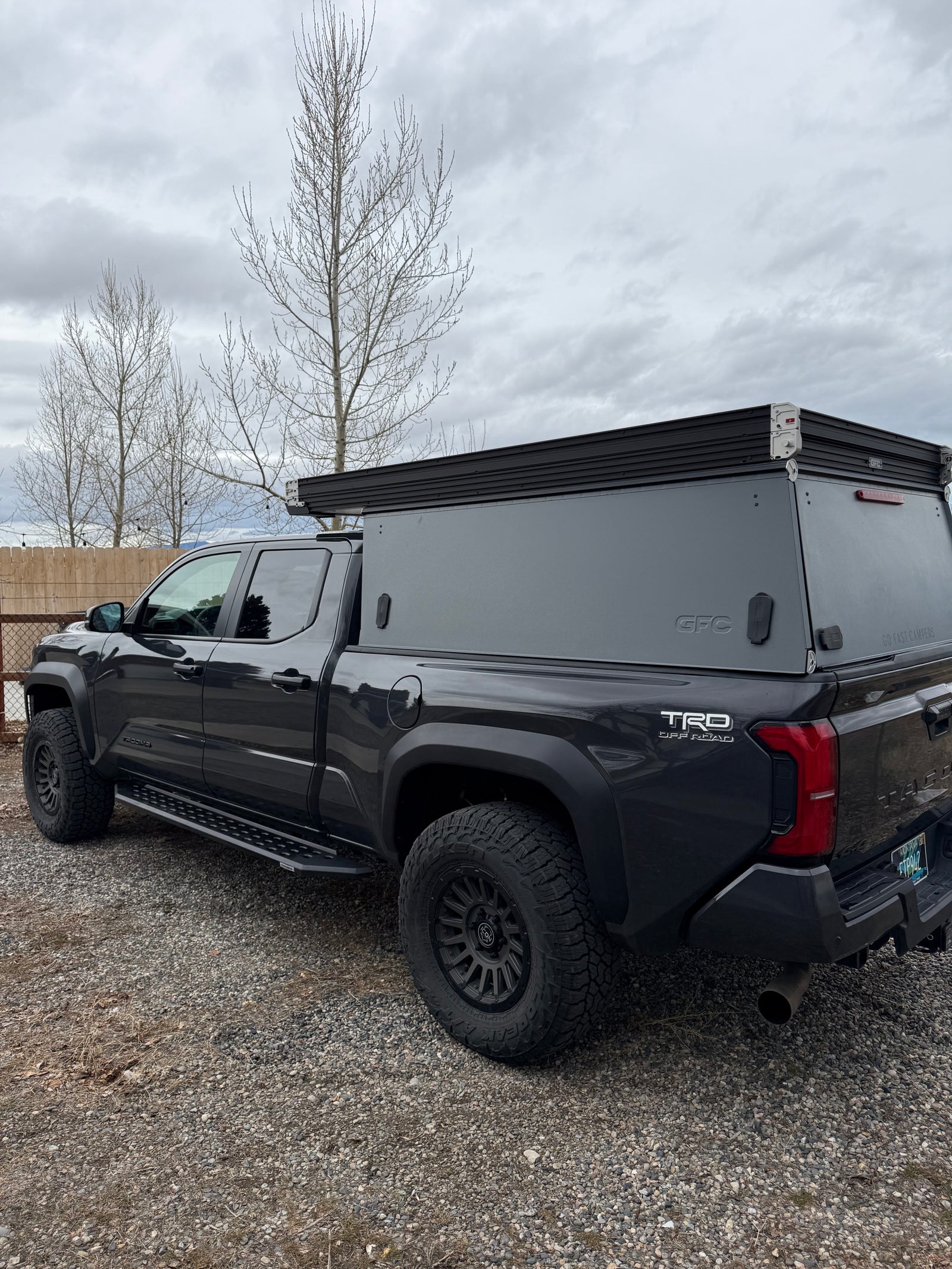 This dark grey Toyota Tacoma truck with a GFC overland camper, equipped with rugged tires, is ready for an RV rental adventure.