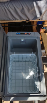 Inside an RV rental portable fridge, showing open lid, bright interior, wire basket, and control panel with digital display.