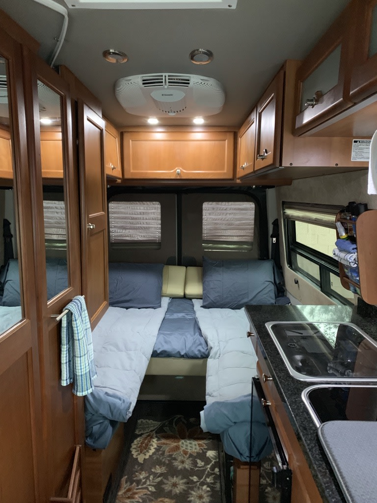  with a sleek black glass top and control knobs for easy cooking.|Compact RV rental interior with dual sleeping areas — photo 2