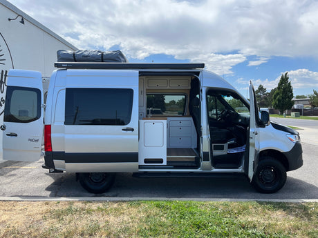 Custom silver Sprinter van, perfect for RV rental, with rooftop tent & open side revealing its organized camper interior.