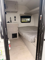 Step into this modern RV rental: a compact interior with a checkered bed, functional kitchen, and light wood floors.