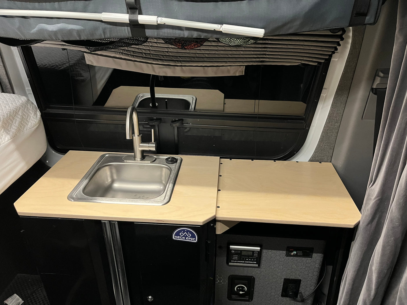 This rv rental features a compact camper van kitchen with a sink, countertop, and solar charging system for off-grid living.