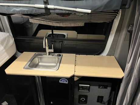 This rv rental features a compact camper van kitchen with a sink, countertop, and solar charging system for off-grid living.