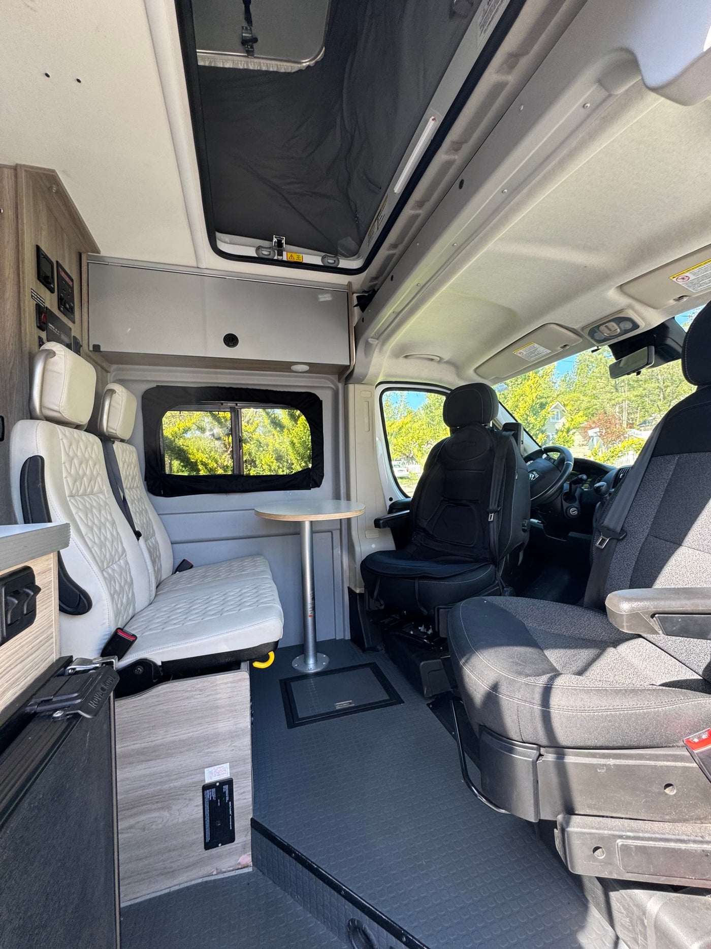 Modern rv rental interior with white quilted passenger seats, dining table, and driver's cabin. — photo 5