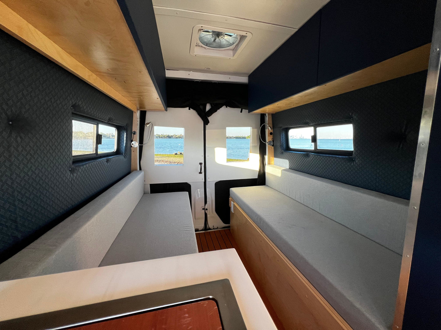 Bright rv rental camper van interior: comfortable seating, ceiling fan, and scenic water views from the windows. Ideal for travel.