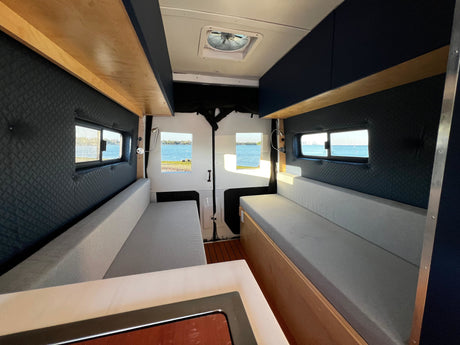 Bright rv rental camper van interior: comfortable seating, ceiling fan, and scenic water views from the windows. Ideal for travel.