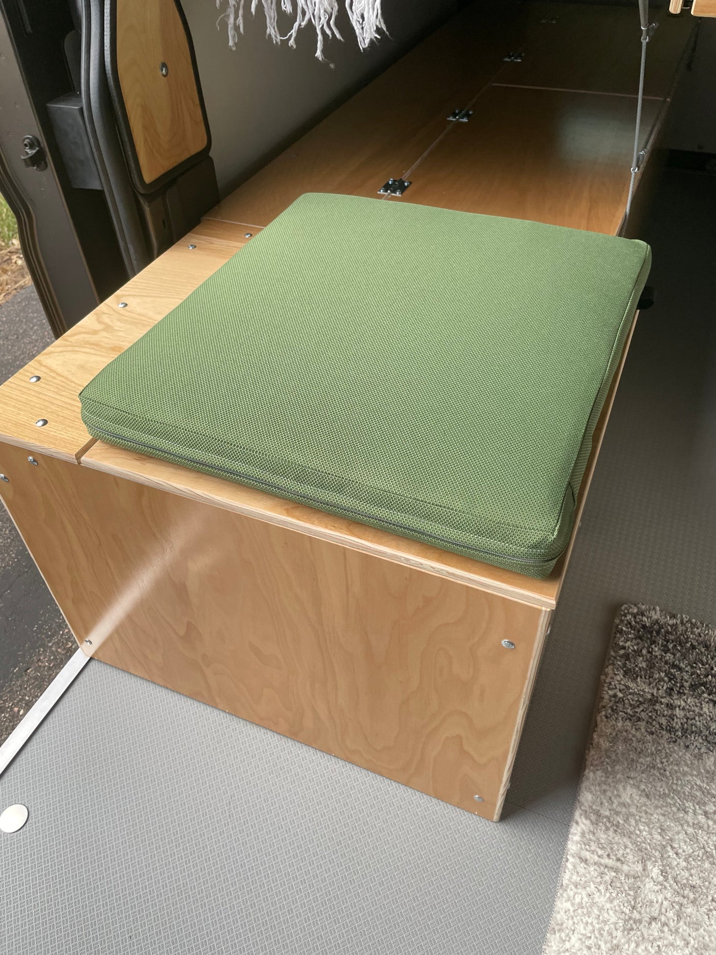 Cozy RV rental interior: custom plywood bench with a green cushion, ideal for seating or a bed in this camper van.