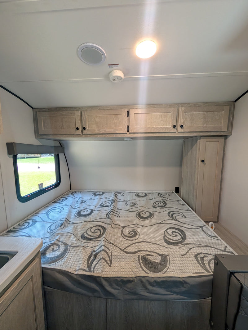 Inside an RV rental: a neat bedroom with a patterned mattress, wooden overhead cabinets, and a side window. — photo 11