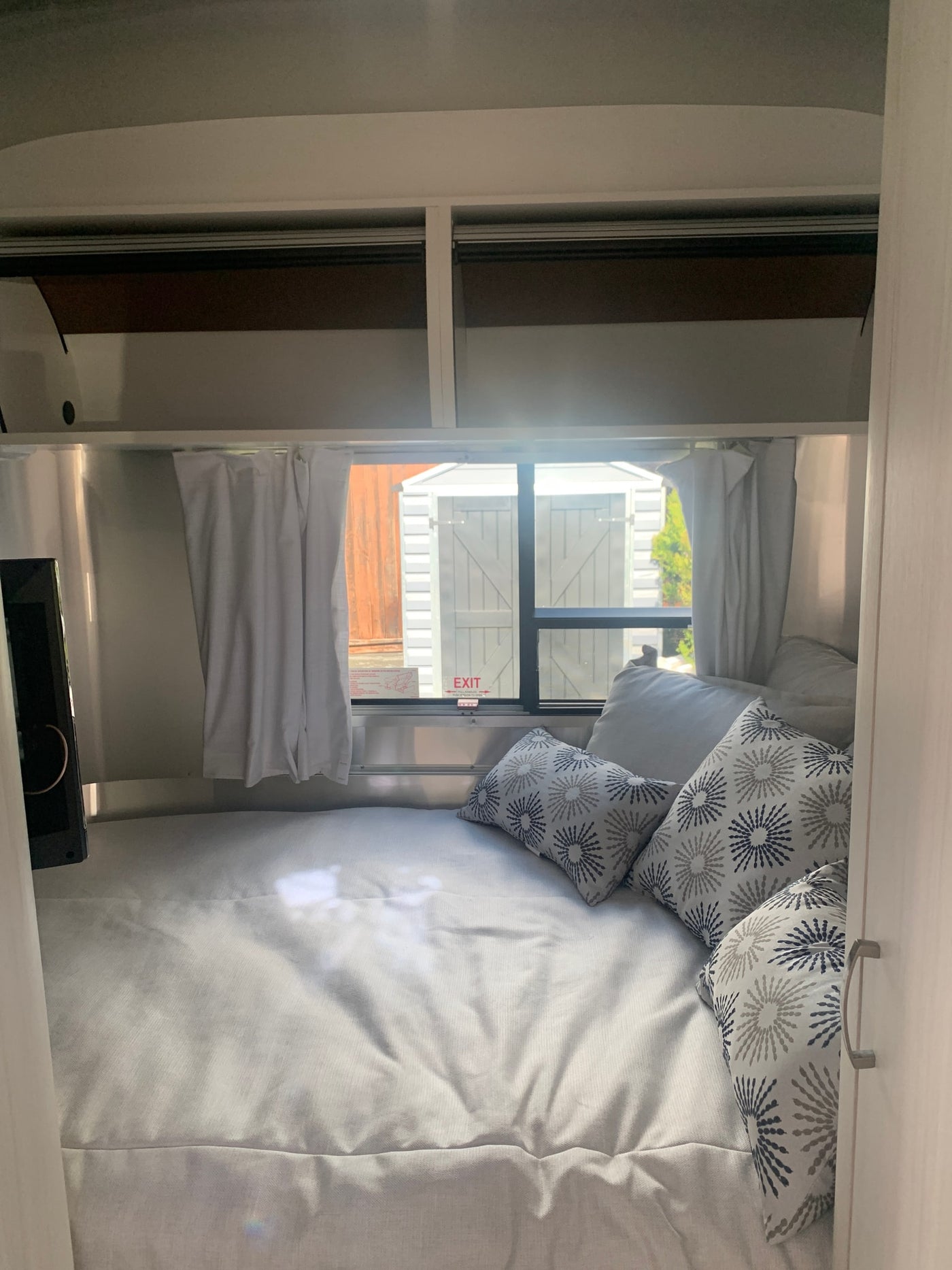 RV rental cozy sleeping area: bed with sunburst pillows, TV, overhead storage, and a bright window. — photo 4