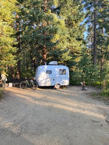 This teardrop RV rental camper, nestled in a quiet forest campsite, offers a perfect outdoor adventure getaway.