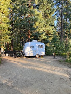 This teardrop RV rental camper, nestled in a quiet forest campsite, offers a perfect outdoor adventure getaway.