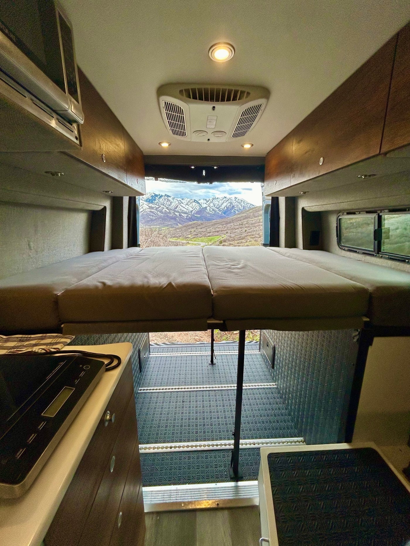 RV rental interior: raised bed with mountain view from back, overhead AC, and kitchenette area. — photo 19