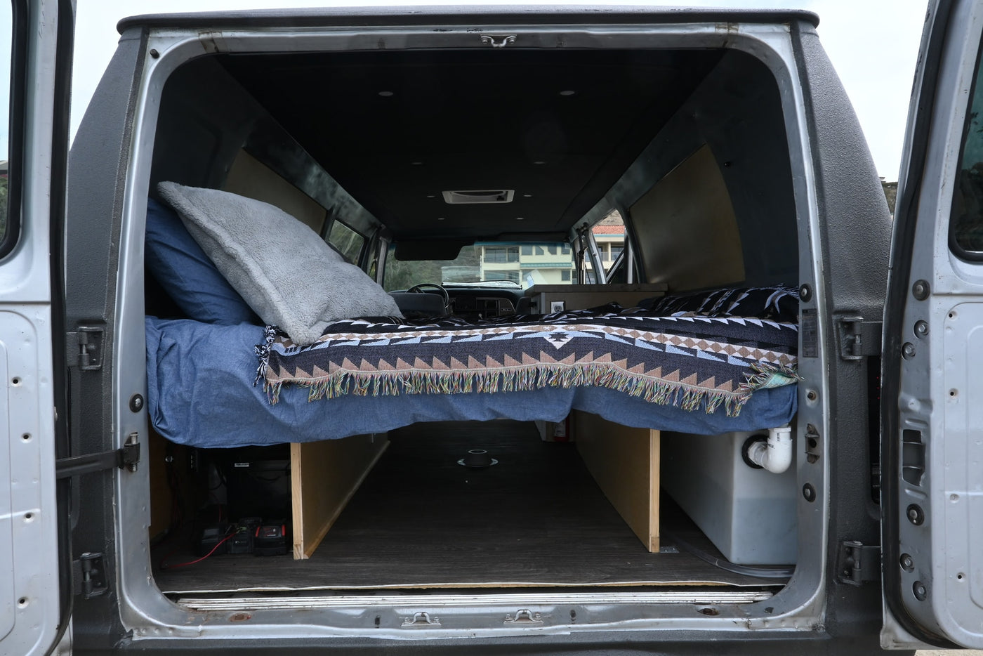 Cozy rv rental camper van interior, seen from the rear doors, showcases a bed, under-bed storage, and custom build details. — photo 5