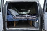 Cozy rv rental camper van interior, seen from the rear doors, showcases a bed, under-bed storage, and custom build details.