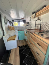 RV rental interior: cozy camper van featuring a bed, kitchenette, mini-fridge, and built-in seating.