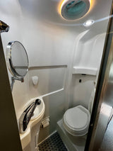 Functional RV rental bathroom featuring a compact toilet, sink with mirror, and an integrated shower area.