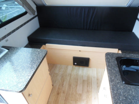 RV rental interior featuring a convertible black bench bed, compact kitchen with sink, and light wood cabinetry.