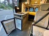 Interior of an RV rental showing kitchen with fridge, stove, sink, and passenger seat, with Golden Gate Bridge view outside.
