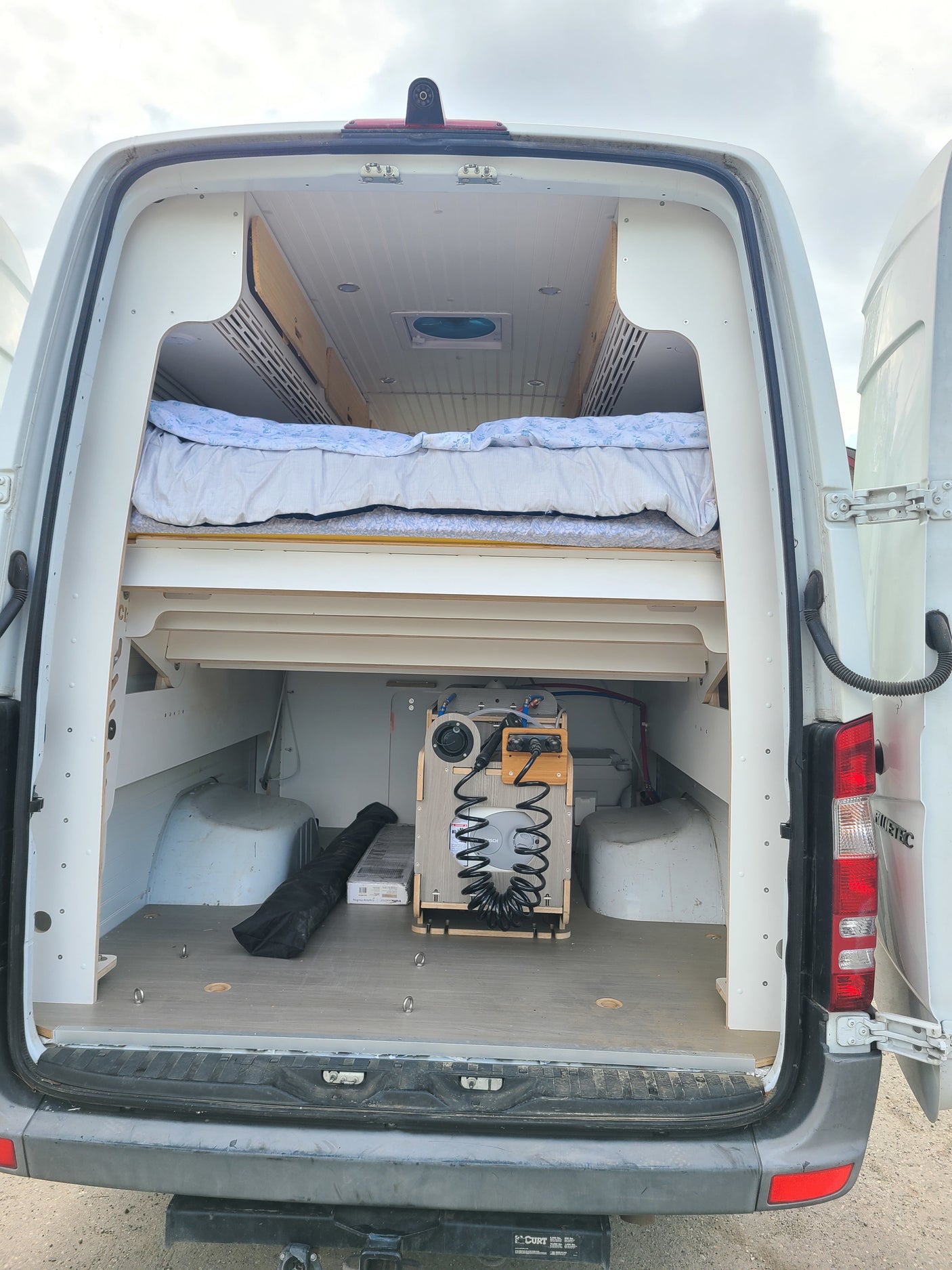 RV rental van interior: custom bed, under-bed storage, and a practical portable water system in the open rear hatch.