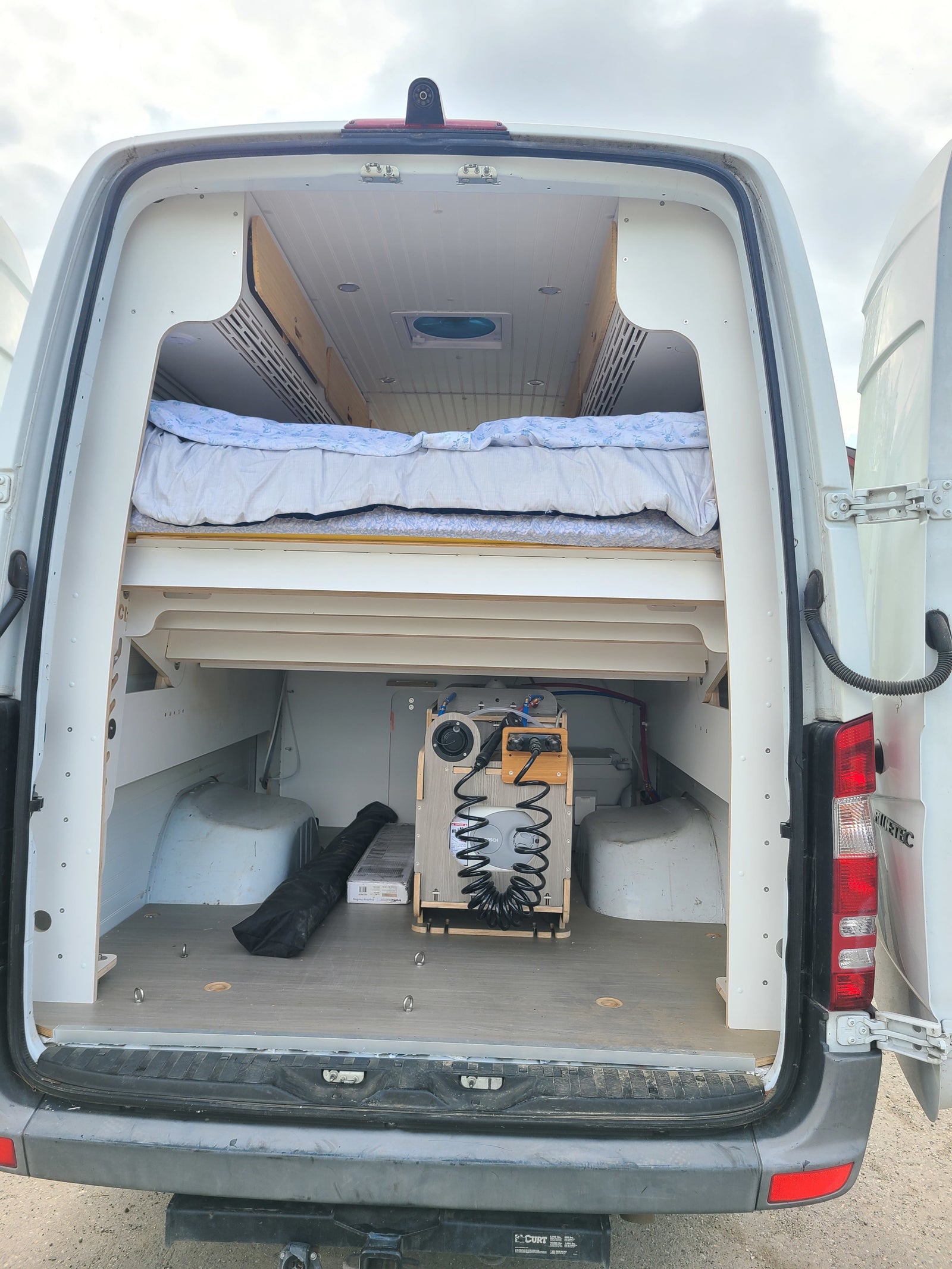 RV rental van interior: custom bed, under-bed storage, and a practical portable water system in the open rear hatch.