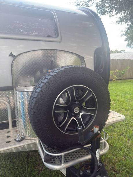 Rear of a compact RV rental, showing a robust off-road spare tire, hitch, and aluminum utility box. Perfect for adventure.